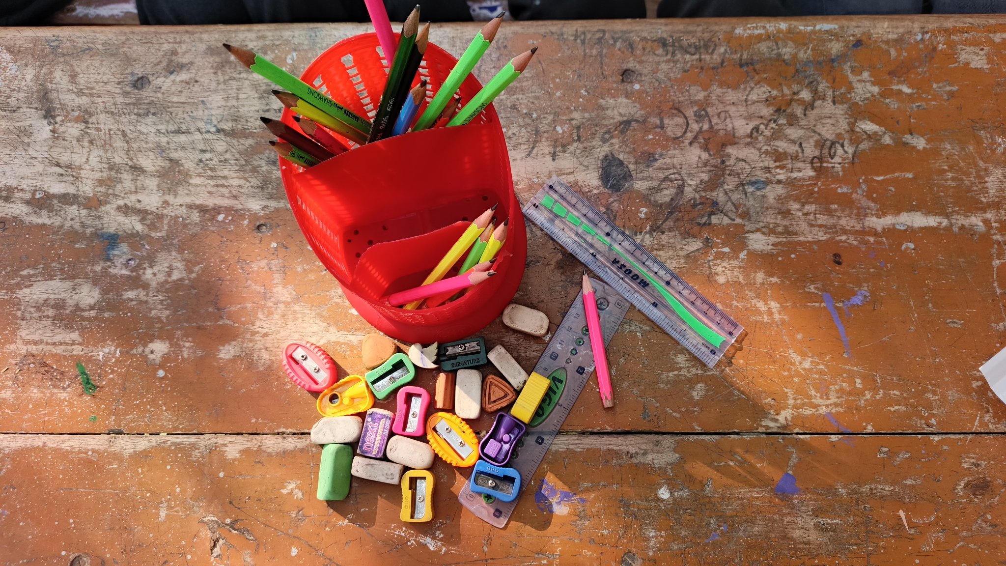 The Class 2 pencil bank: one red bin holds the whole class's pencils, with the shared erasers, sharpeners and rulers beside it on the desk.